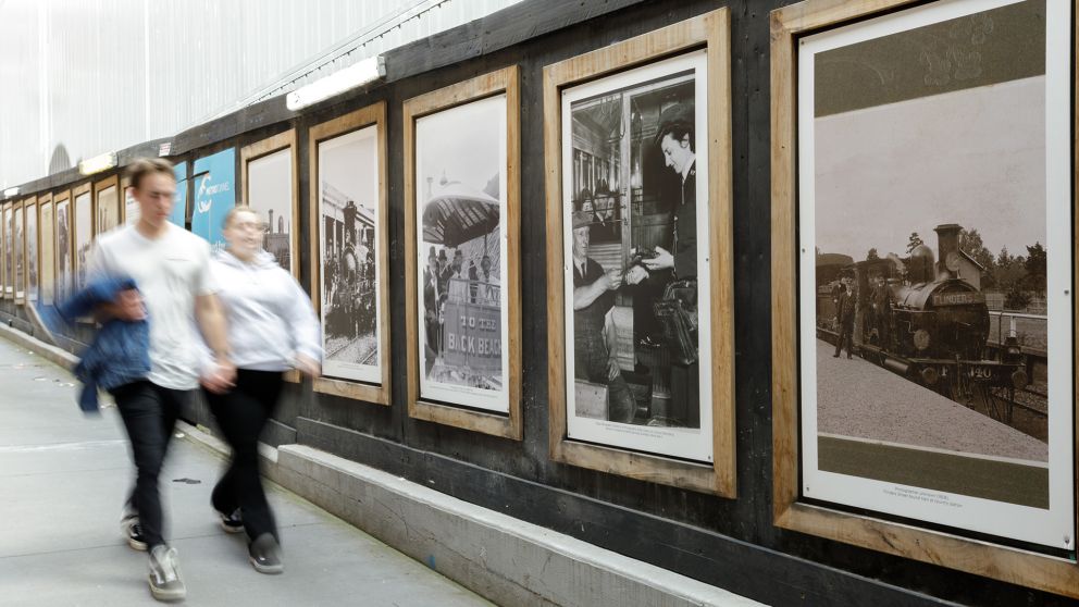 Two people walk past old photographs on display in wooden frames