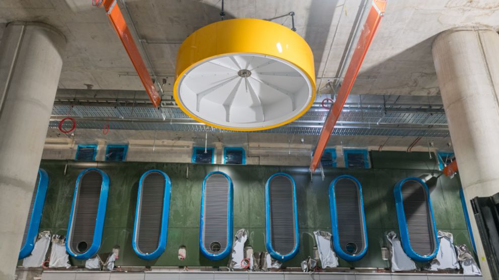 A yellow drum light on the ceiling and 6 blue ventilation shafts on a green wall.