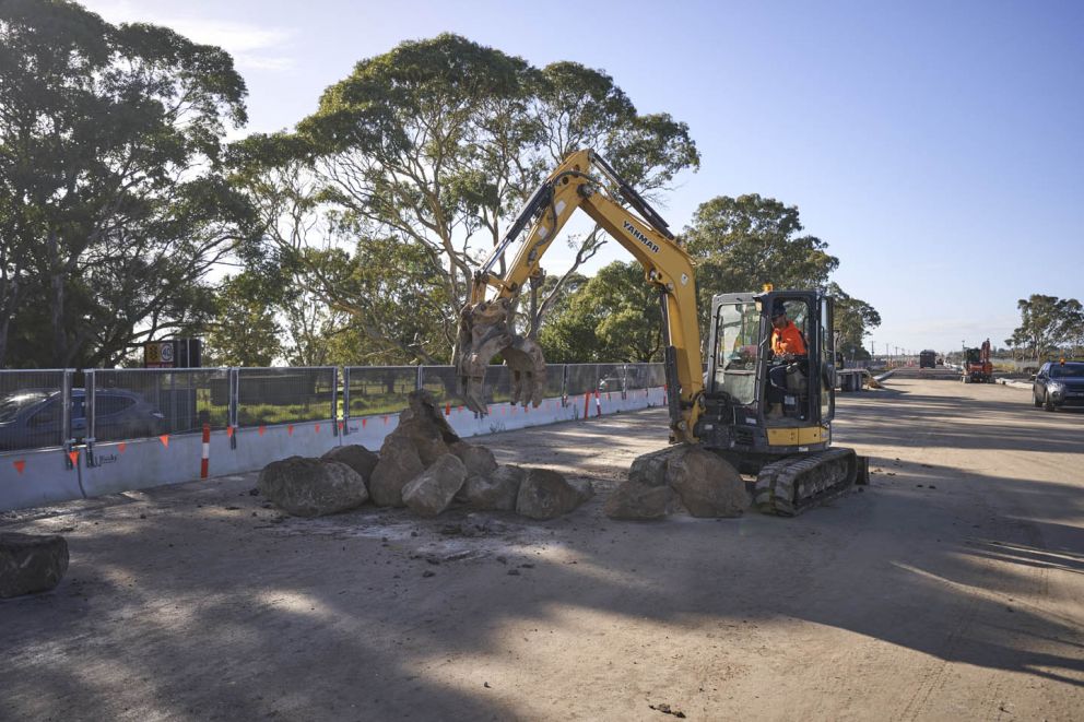 An excavator operator skilfully shaping boulders for rock beaching, the process of safeguarding stormwater banks from erosion with strategic placement of rocks.