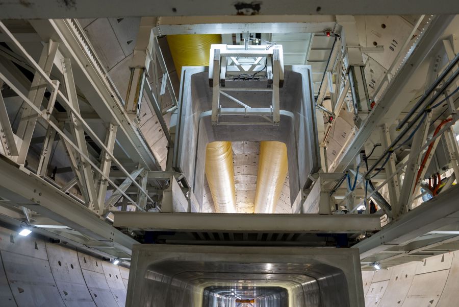 Inside view of a massive tunnel structure with machinery and overhead pipes.