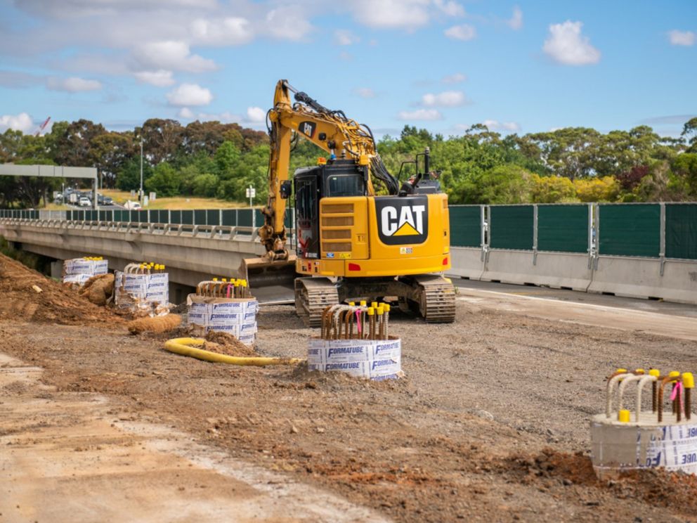 September 2020 Preparation of pile caps at Ferntree Gully Road. The image shows an excavator on site with the concrete barriers in the background.