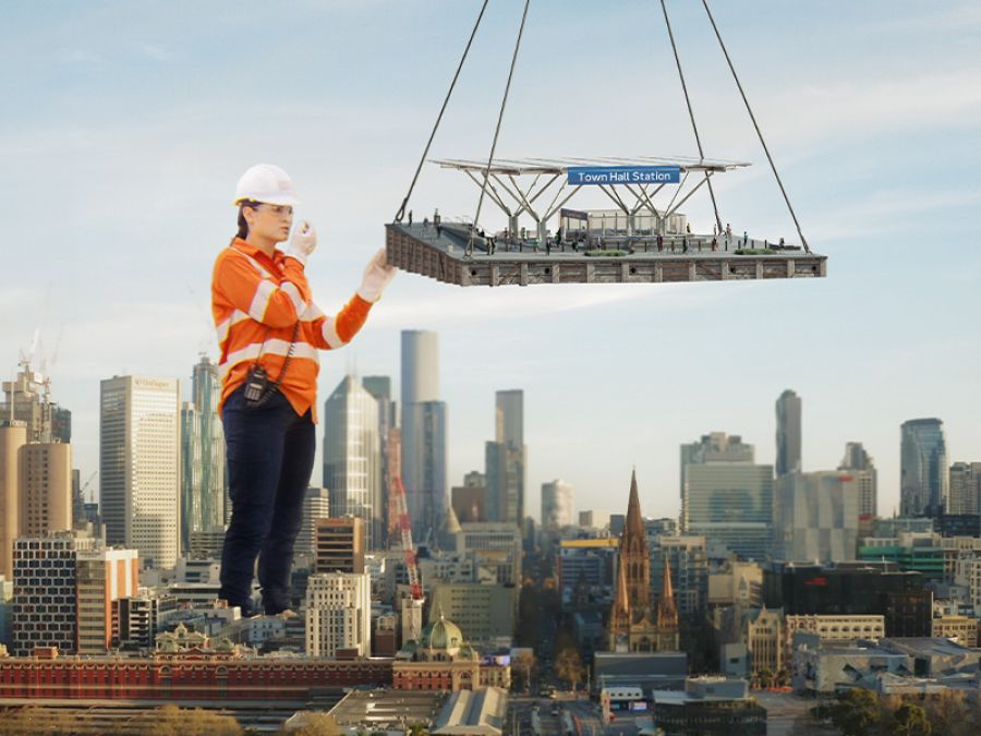 A giant construction worker moves a train station canopy into place.