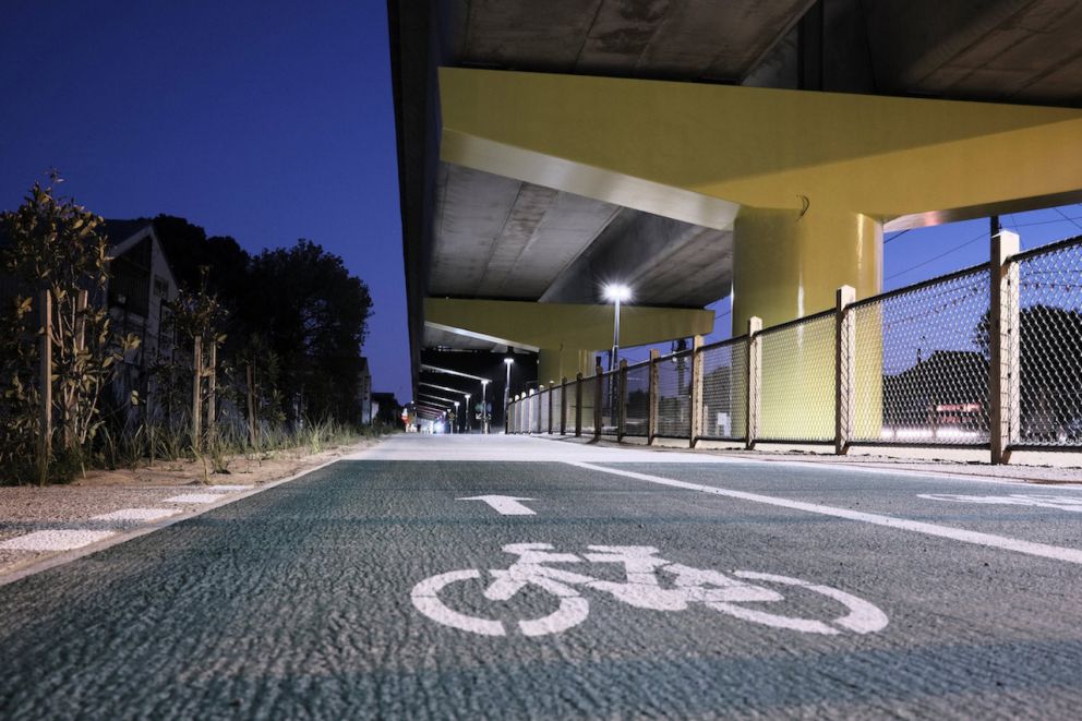 Bike path signage on ground with a large yellow pylon and dog park in the background.