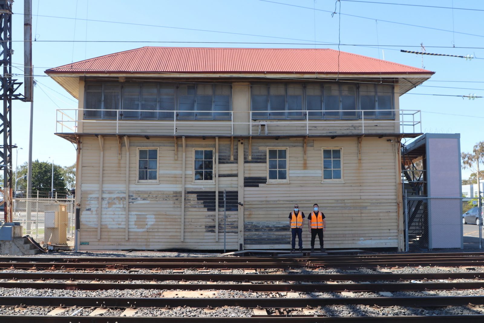 Two workers standing in front of an old weatherboard building near the train lines.