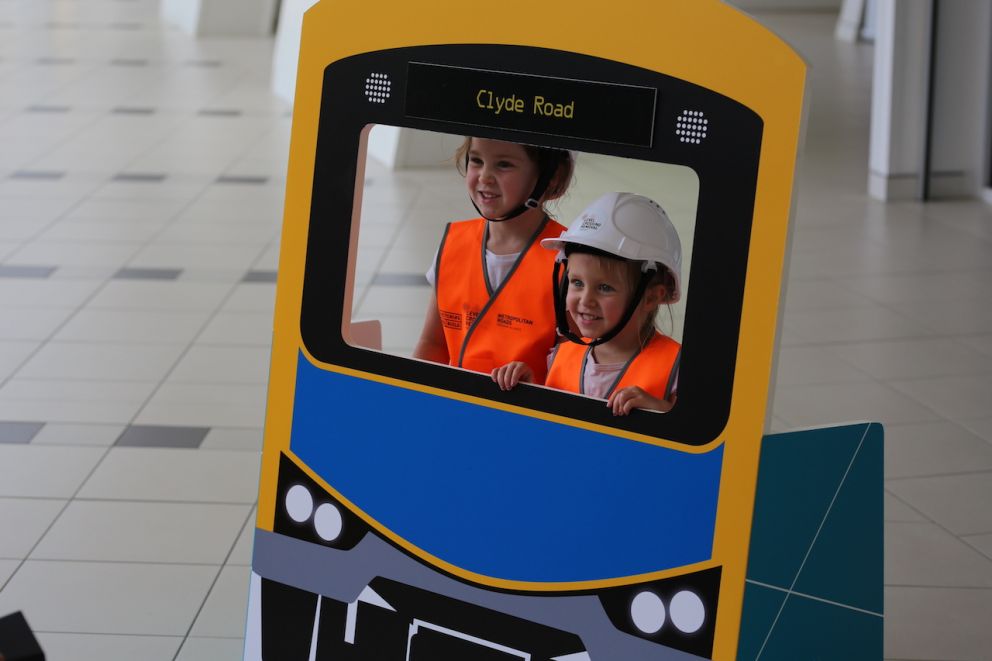 Two children standing behind a cut out of a train.