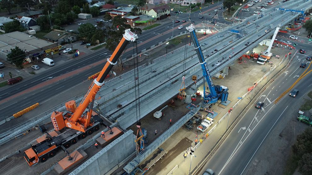 Cranes lift an L-beam onto the rail bridge