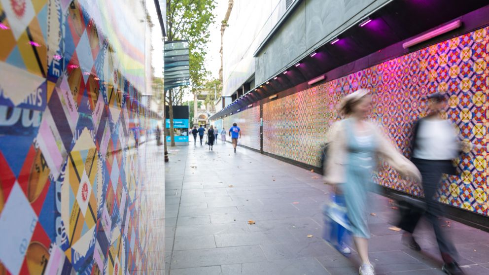 Two people walking towards the camera next to Elizabeth Gower's colourful artwork
