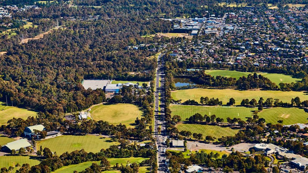 Aerial view of Bulleen Road with many buildings, trees and sporting ovals.