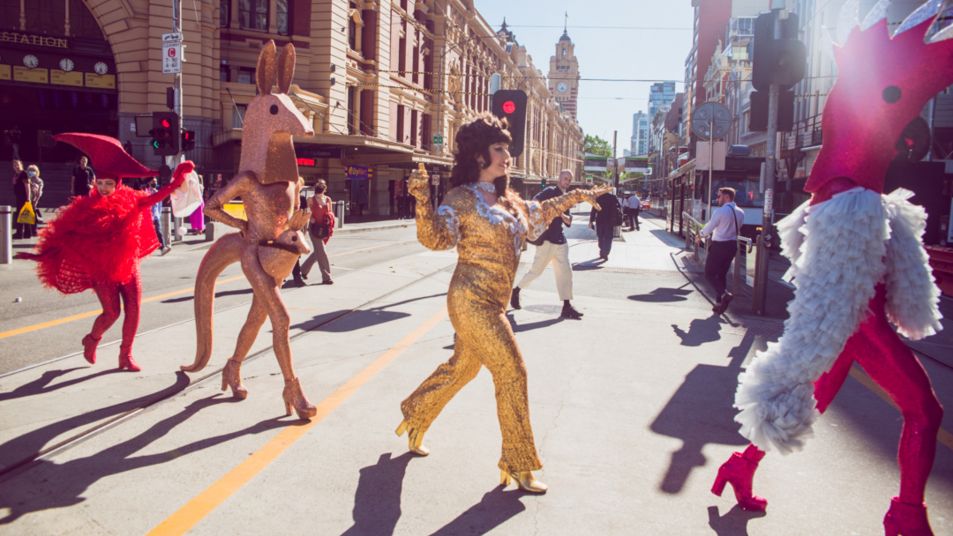 Performers dress in colourful and sparkling costumes crossing the road in front of Flinders Street station