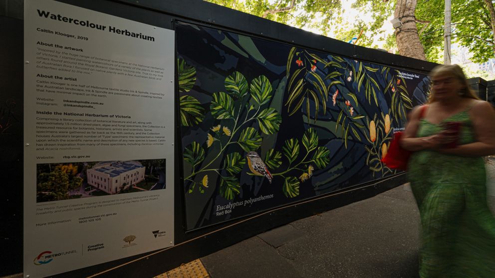 A person walks past a botanical artwork installed on a hoarding wall