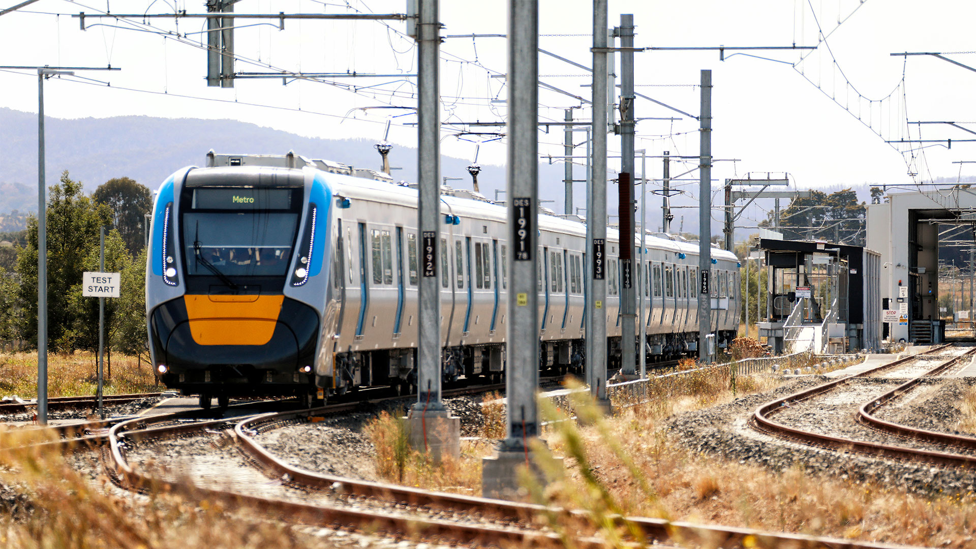 High Capacity Metro Train on Sunbury Line with mountains in the background and scattered plants and trees